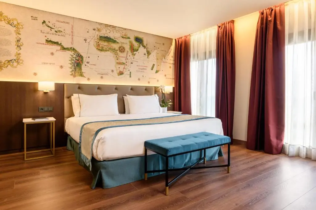 Guest room at Áurea Museum with an antique world map painted on the wall above the bed, wooden floor and deep red curtains