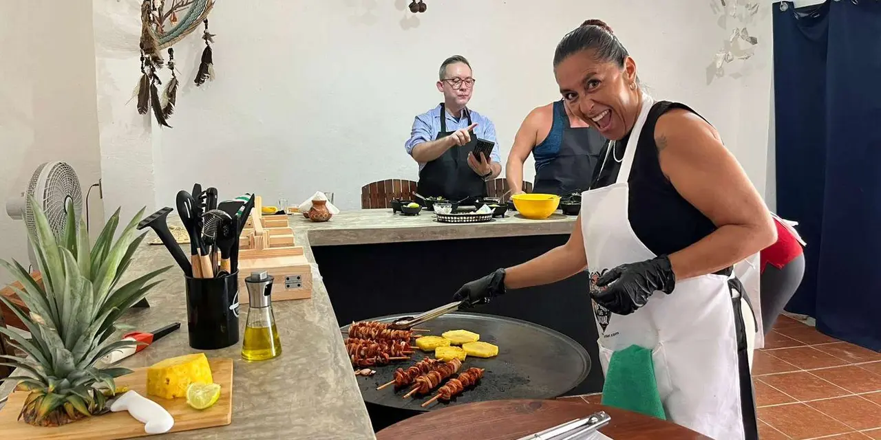 A cook in a white apron turning marinated skewers and pineapple slices on a round griddle while two other guests cook at the counter behind her