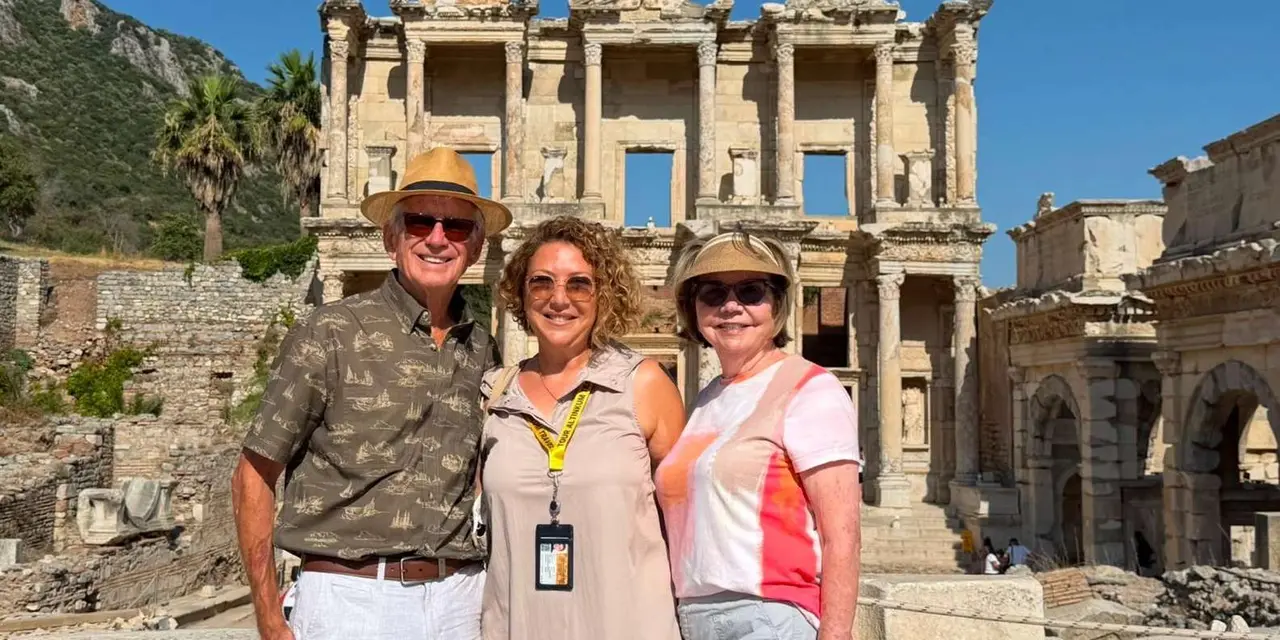 Three visitors in sun hats posing in front of the two-storey marble facade of the Library of Celsus at Ephesus
