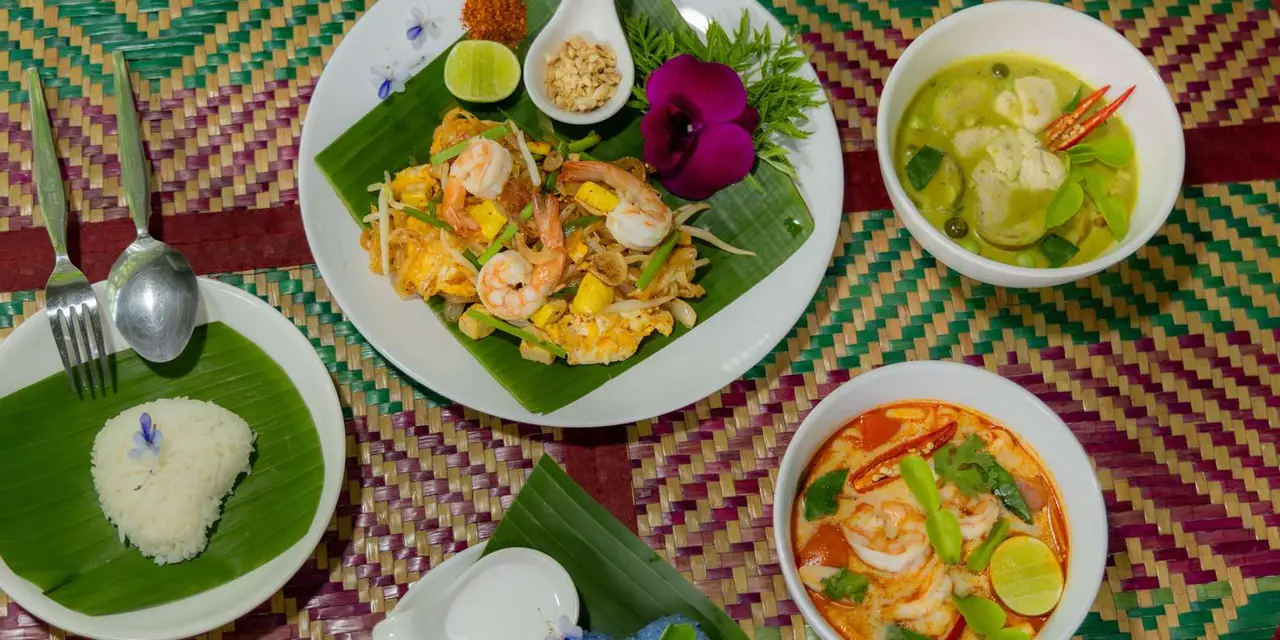 A spread of Thai dishes served on banana leaves on a patterned tablecloth