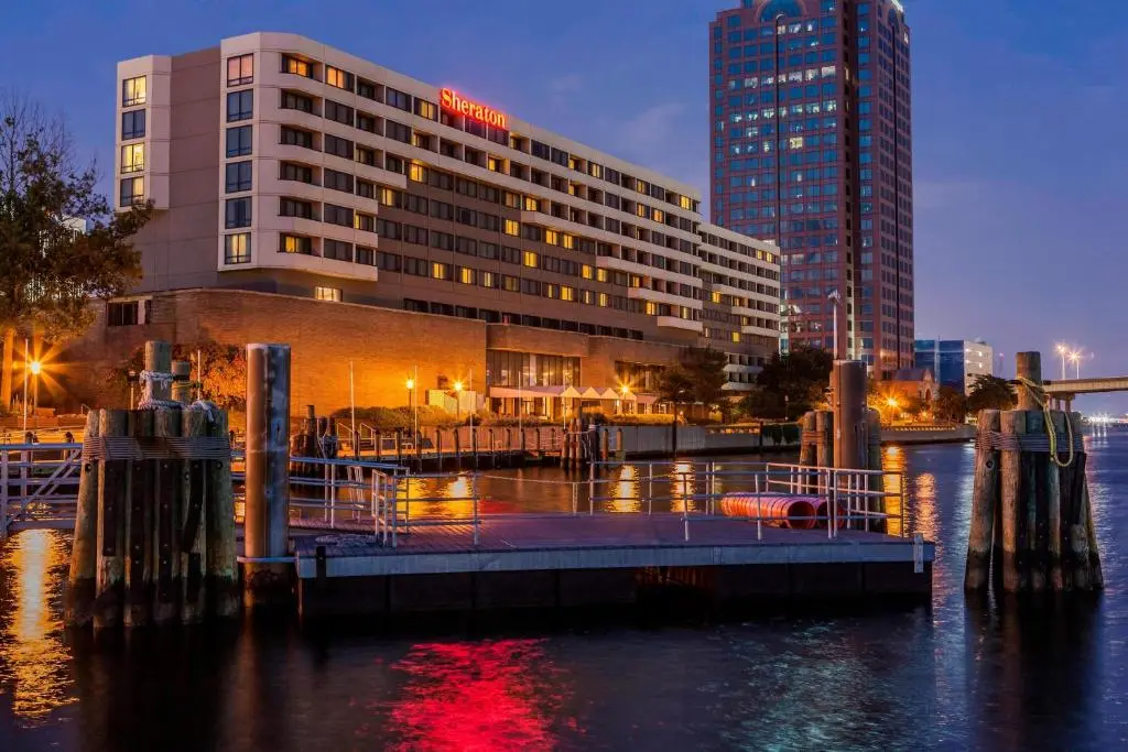 The Sheraton Norfolk Waterside Hotel lit up at dusk on the Elizabeth River, seen from the water past a floating dock