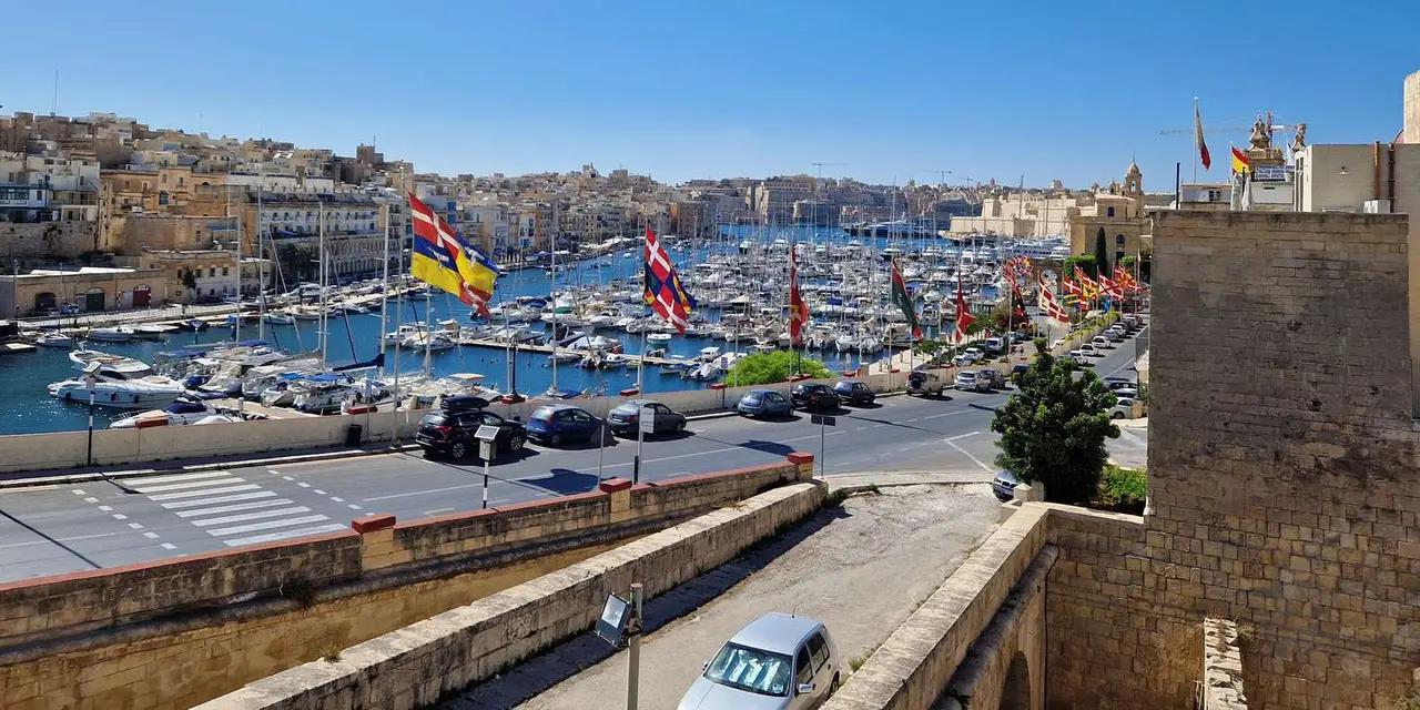 Birgu's yacht marina below the stone buildings of the Three Cities, under a blue sky