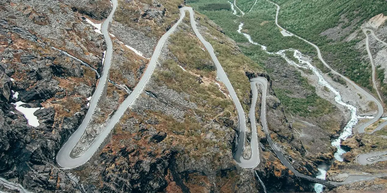 Aerial view of the Trollstigen road zig-zagging down a steep green valley beside a river