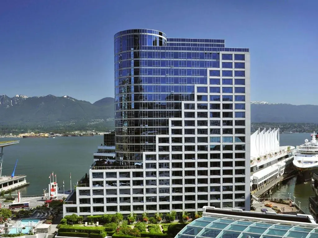 The Fairmont Waterfront's glass tower across from Canada Place, with a cruise ship at the white-sailed terminal and North Shore mountains behind