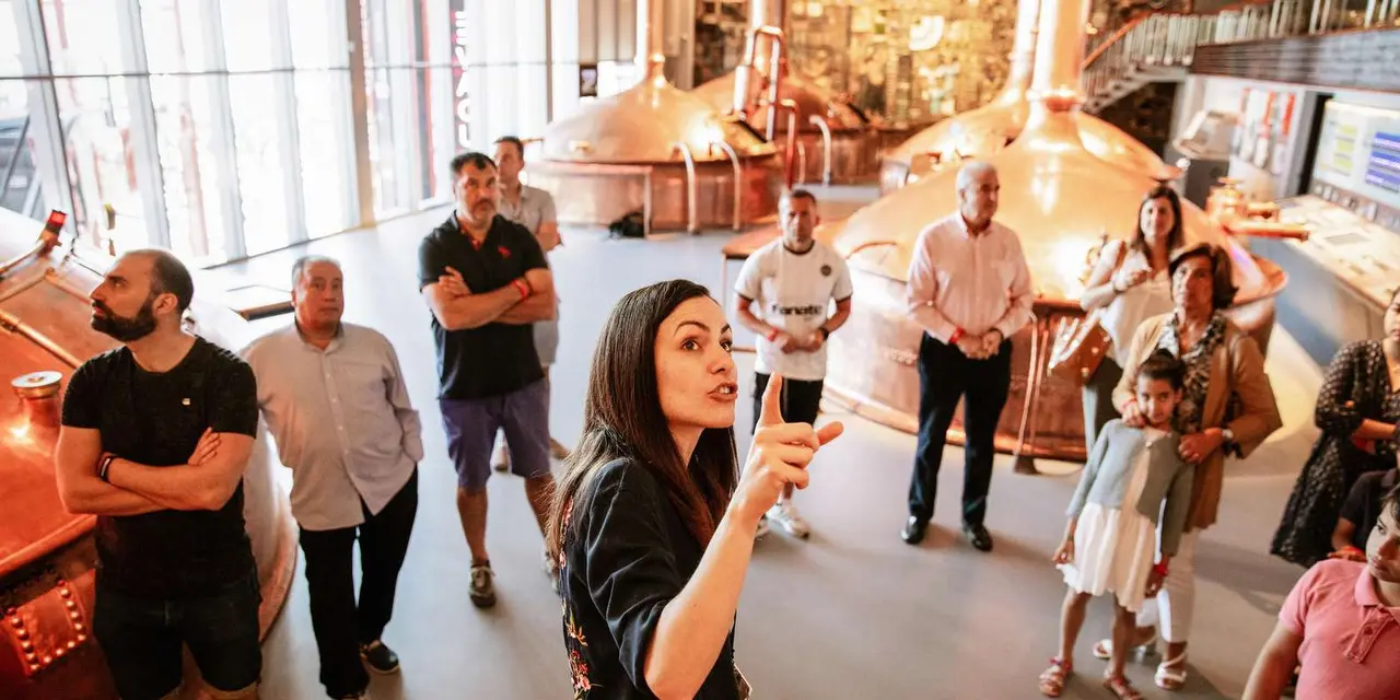 A guide talking to a small group of visitors in front of large copper brewing kettles