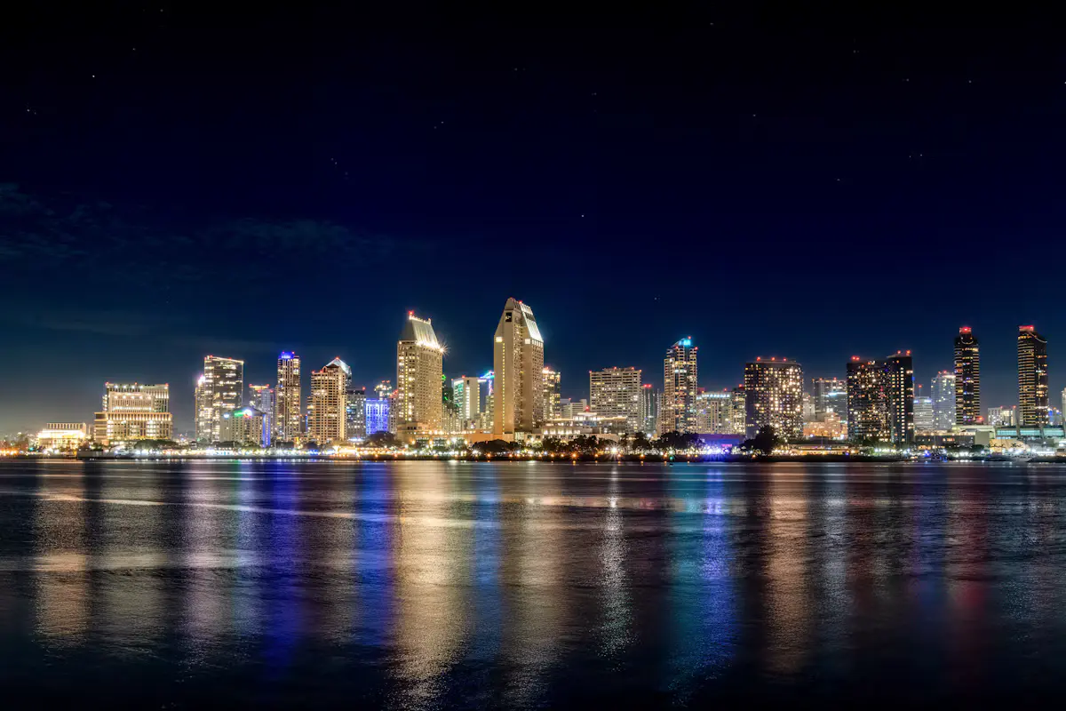 The downtown San Diego skyline lit up at night, its towers reflected in the calm bay water in front