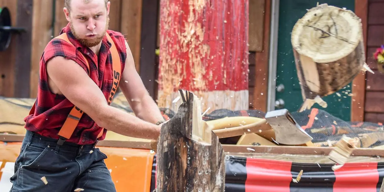 A lumberjack in a red plaid shirt swinging an axe into a log
