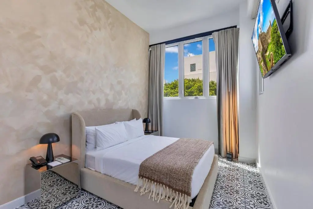 A Hotel Milano guest room with a double bed, patterned tile floor and a window looking out on trees and blue sky