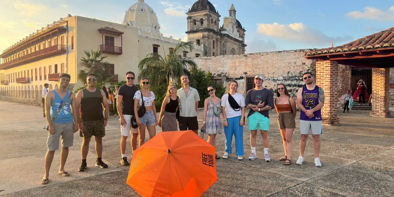 A tour group gathered under an orange umbrella in a sunny plaza, with a domed colonial church behind