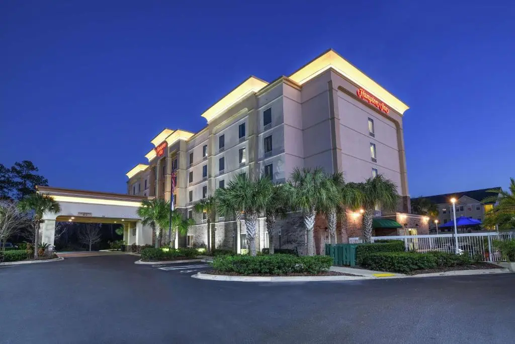 Hampton Inn Jacksonville East at dusk, a lit five-storey hotel with a covered entrance and palm trees along the front