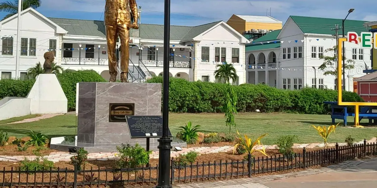 A gold statue on a stone plinth in front of a white colonial building with a green roof