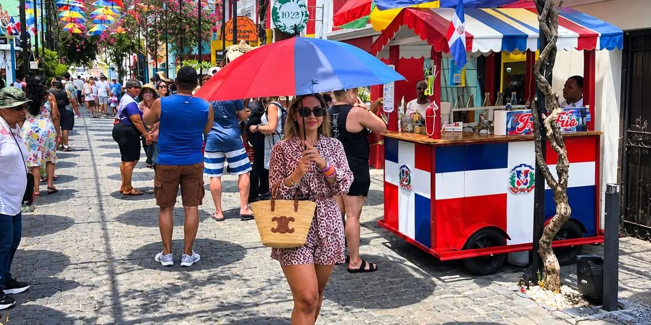 A woman walking past a red, white and blue street cart under colourful umbrellas in Puerto Plata