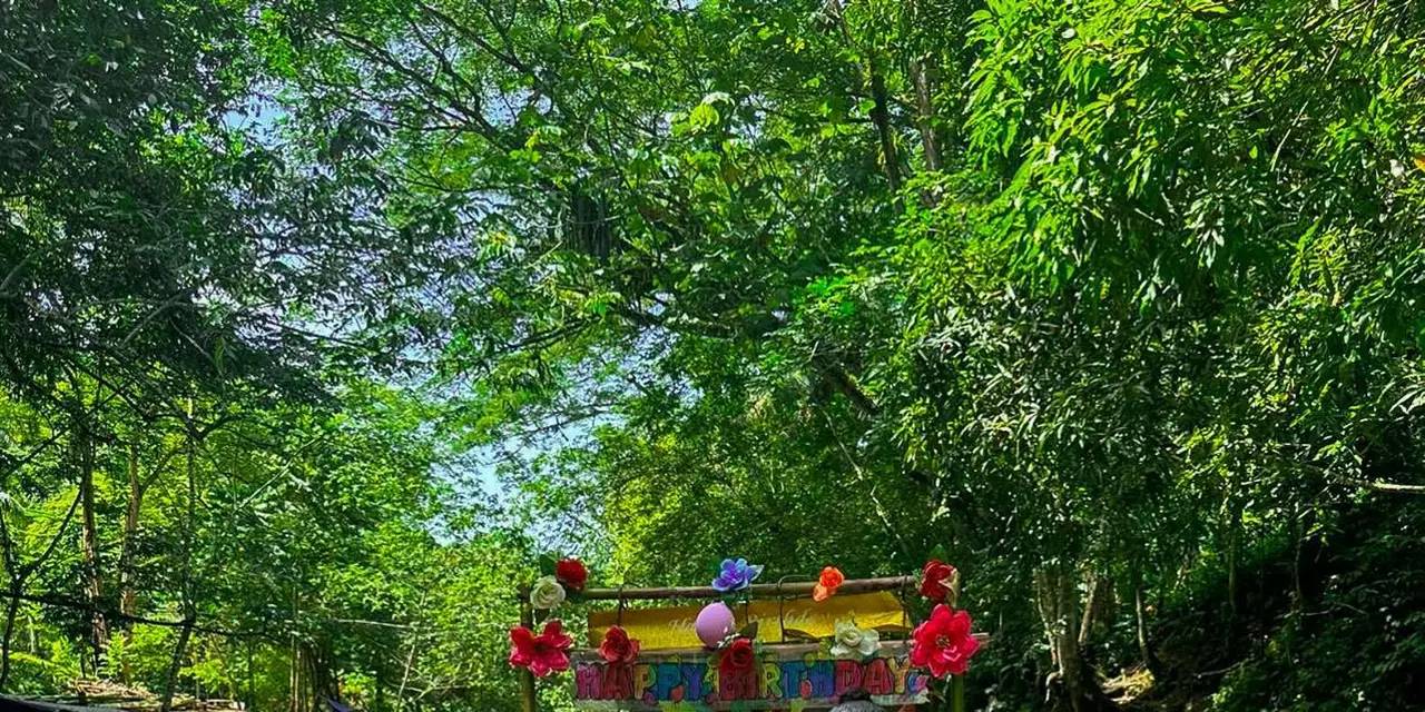 Two women sitting on a flower-decked bamboo raft on a calm green river