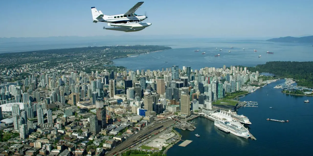 A white floatplane flying over downtown Vancouver, with Canada Place and two cruise ships at the waterfront below