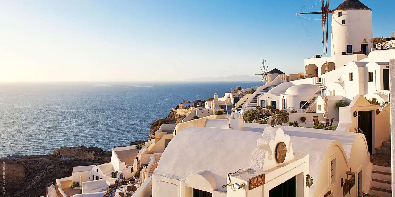Whitewashed Oia houses and a windmill above a calm blue sea in golden evening light