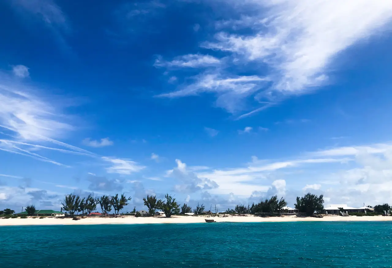 Turquoise sea in front of a low strip of white sand and palm trees on Grand Turk under a deep blue sky