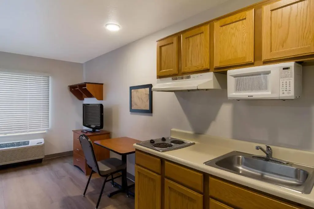 A WoodSpring Suites studio room with a kitchenette, two-burner cooktop, microwave, sink and a small dining table
