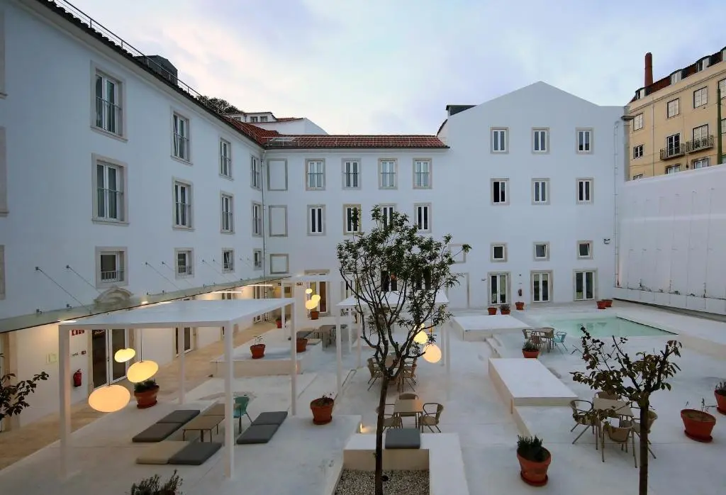 White inner courtyard of Hotel Convento do Salvador at dusk, with lanterns, loungers, potted trees and a small pool