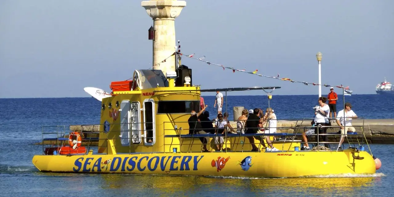 A bright yellow tourist submarine boat marked 'Sea Discovery' with passengers on deck, beside a lighthouse tower on the water