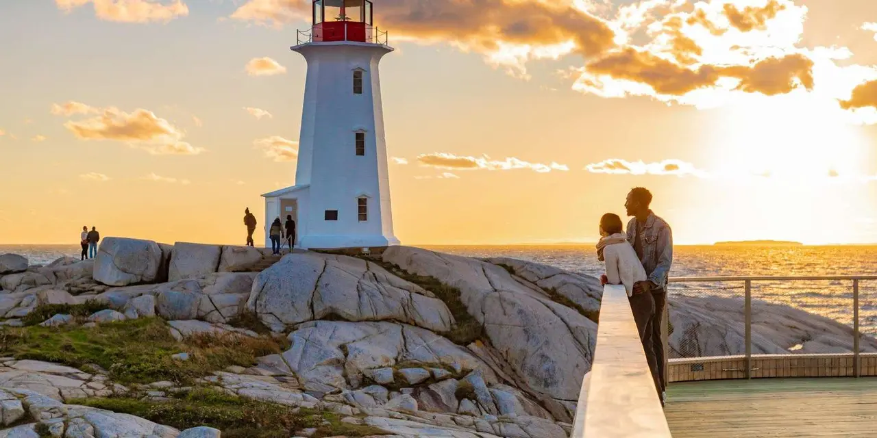Peggy's Point Lighthouse on its granite point at sunset, with a couple in front