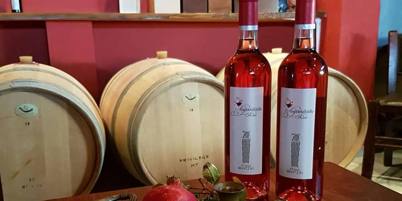Bottles of rosé wine standing in front of oak barrels, with pomegranates in the foreground