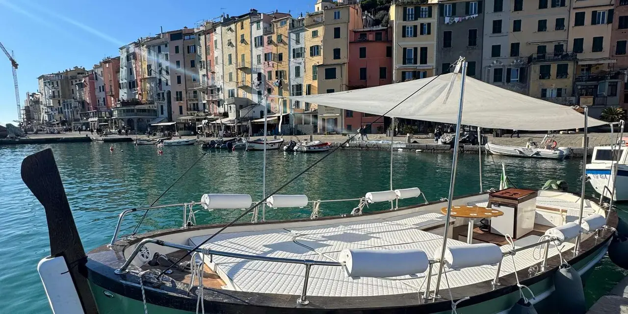 A canopied wooden boat moored in front of Portovenere's pastel harbour houses