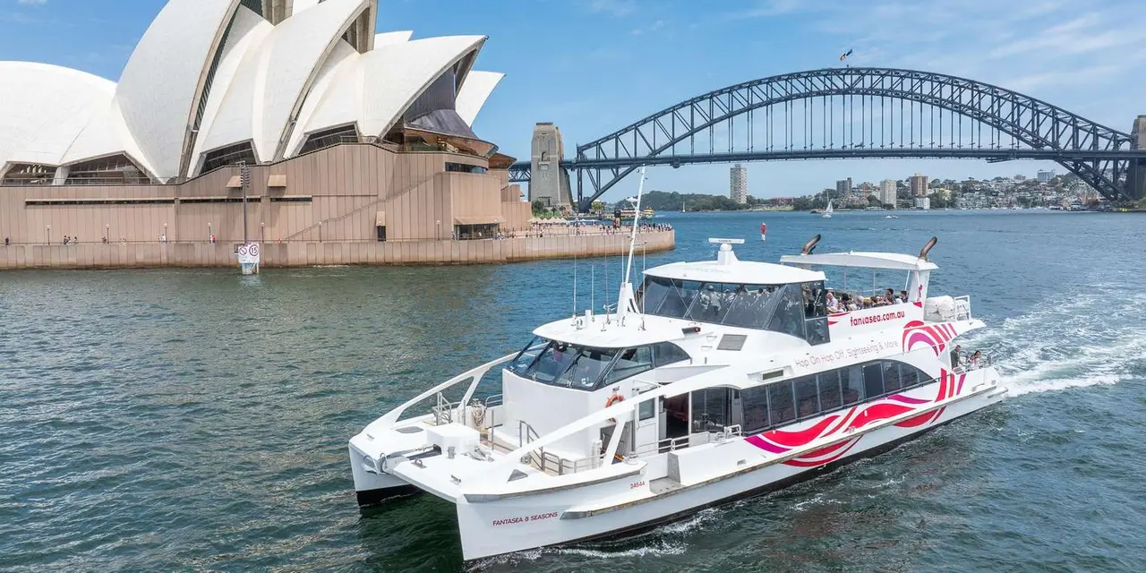 A white catamaran cruising on the harbour in front of the Opera House and the Harbour Bridge