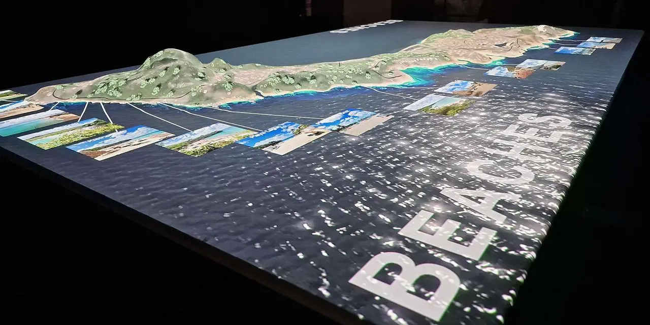 A large illuminated relief map of Curaçao's coastline with photo panels and a 'Beaches' label