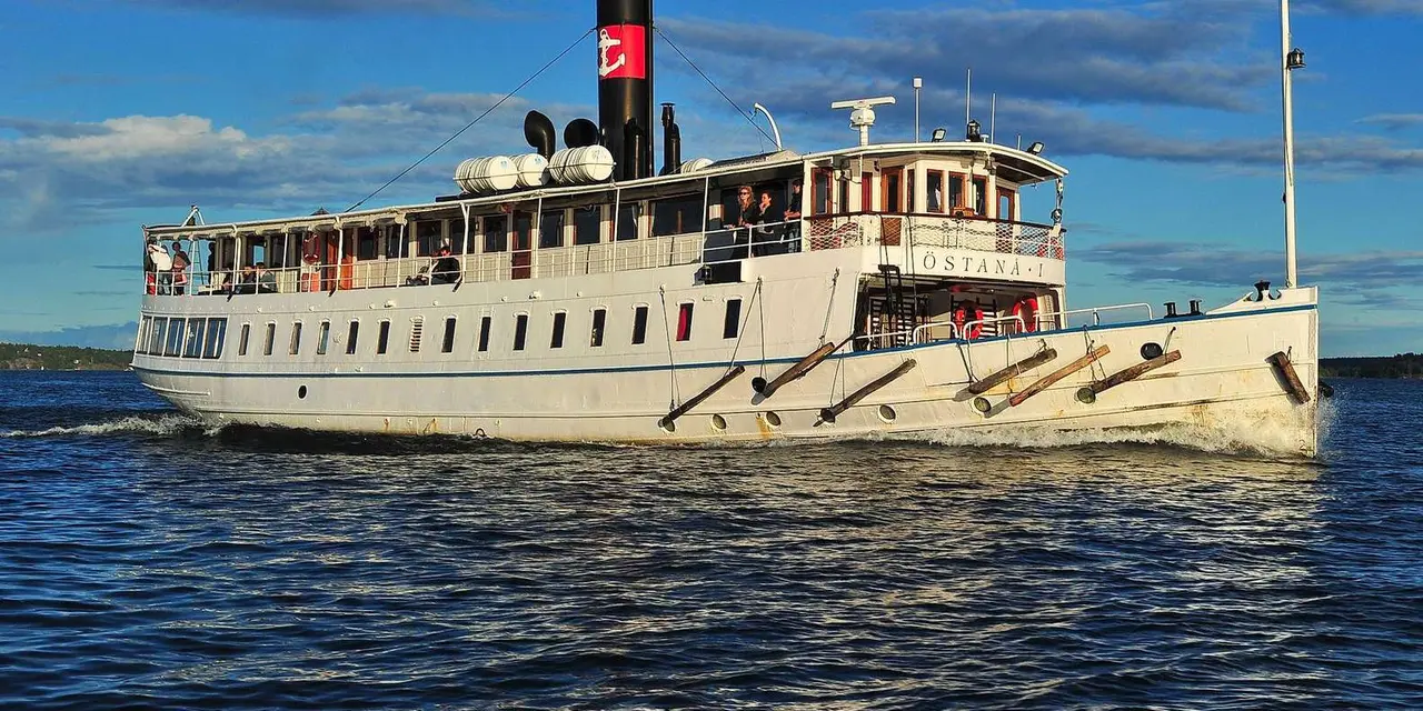 A white steamship with a black funnel and the name Östanå on its hull cruising on open blue water