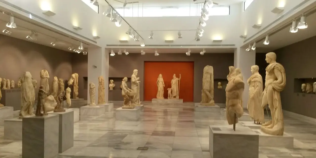 A museum gallery of white marble statues in front of a terracotta-coloured wall