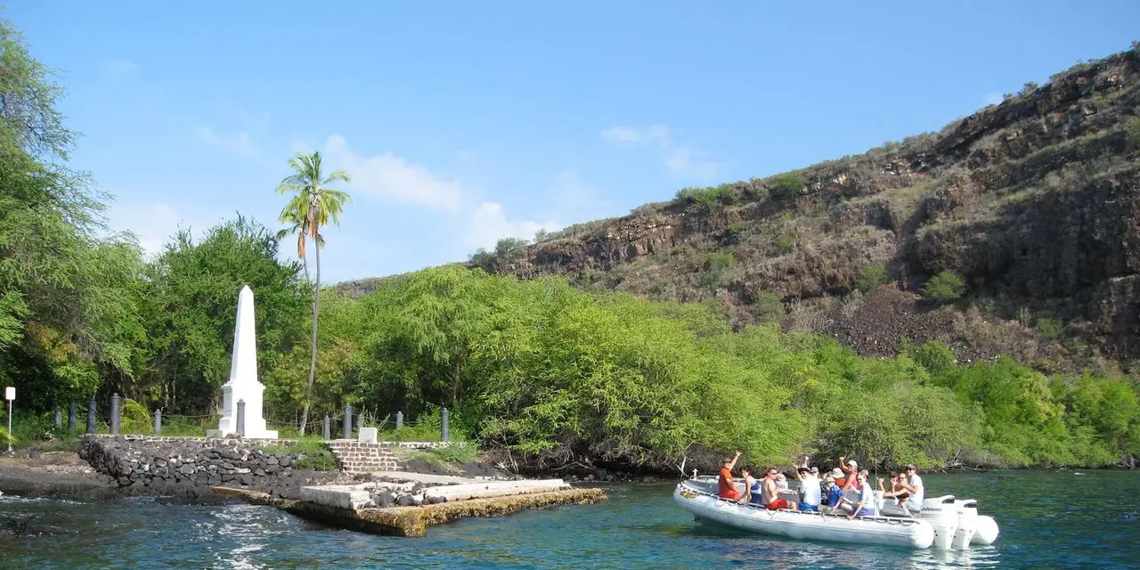 A small tour boat beside the white Captain Cook Monument and its landing in clear blue water