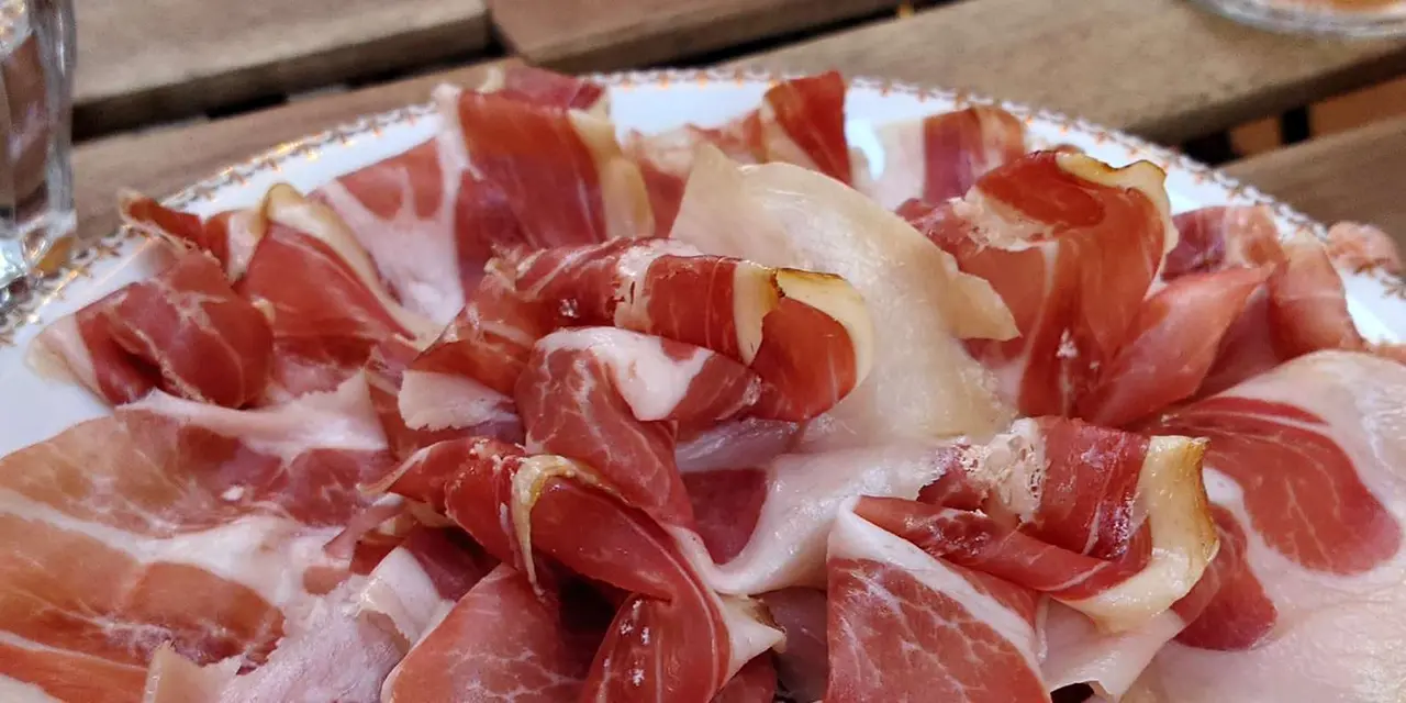 A plate of thinly sliced Corsican cured ham on a wooden table