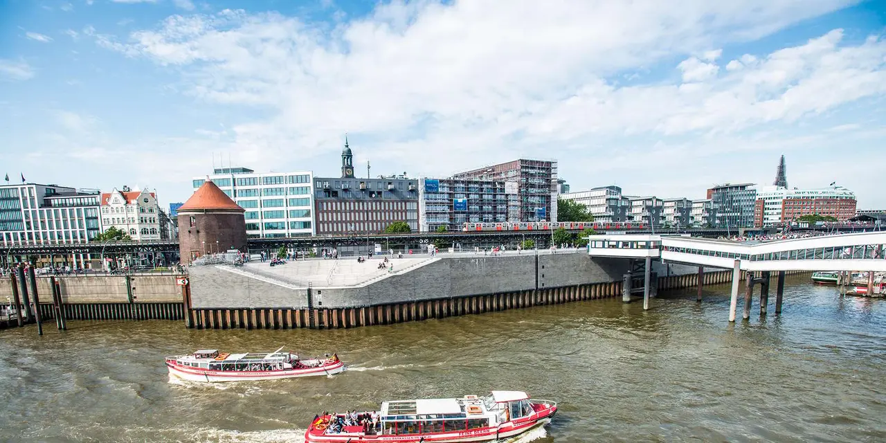 Two pink harbor boats on the Elbe in front of a stepped quay, a brick tower and a church spire on the Hamburg waterfront