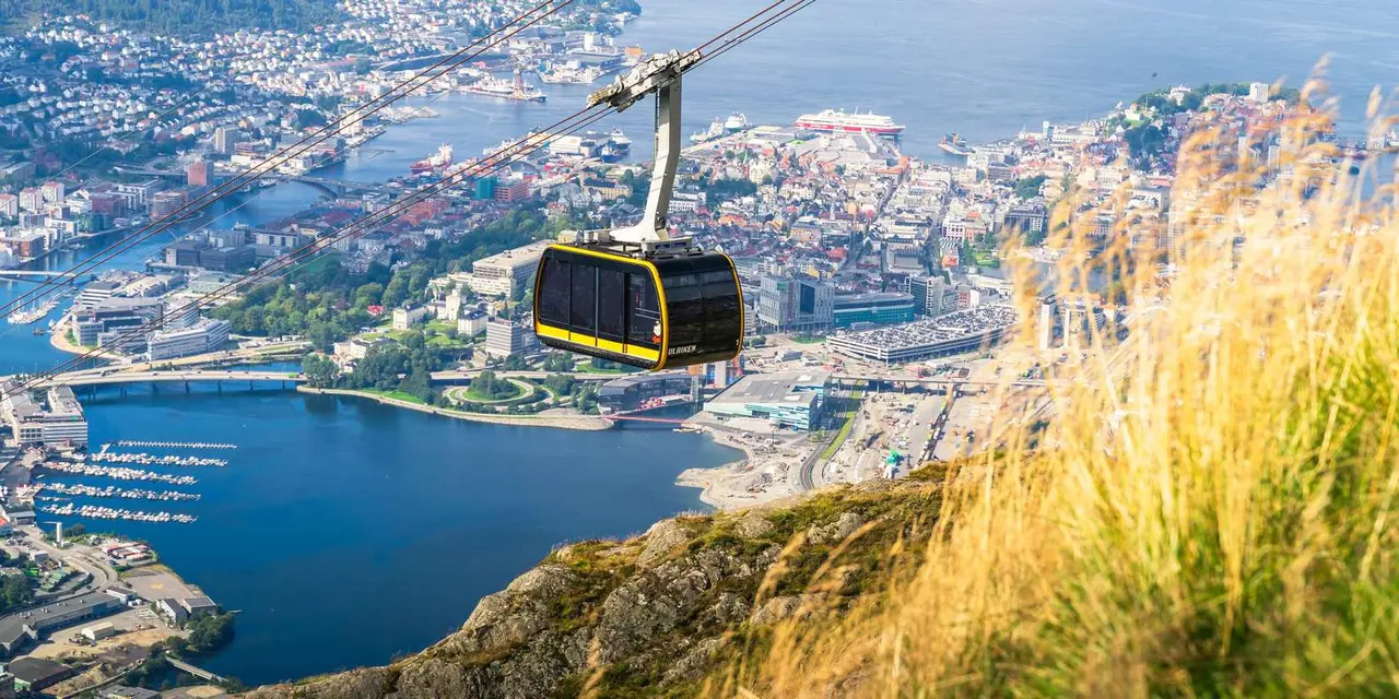 A yellow cable car cabin high above Bergen, with the city, harbour and fjord spread out below