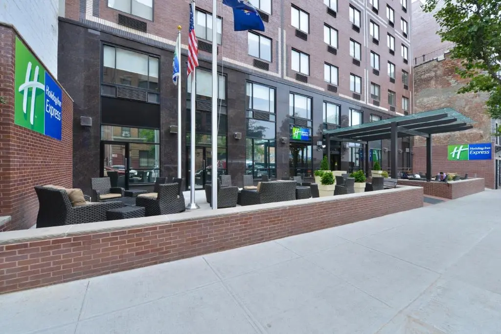 The Holiday Inn Express entrance on West 48th Street, with flags, a canopy and a brick-walled patio with outdoor seating