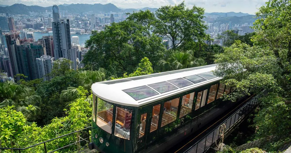 A green Peak Tram car climbing through trees with the skyline behind