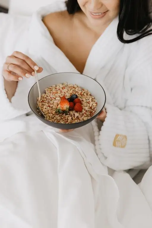 A guest in a white Pan Pacific robe eating a bowl of granola with berries in bed
