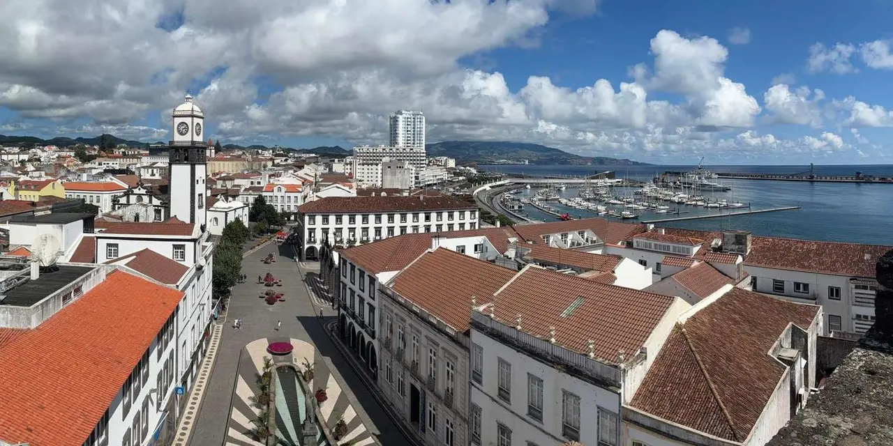 Ponta Delgada's white buildings and red roofs seen from above, a clock tower rising over a long square