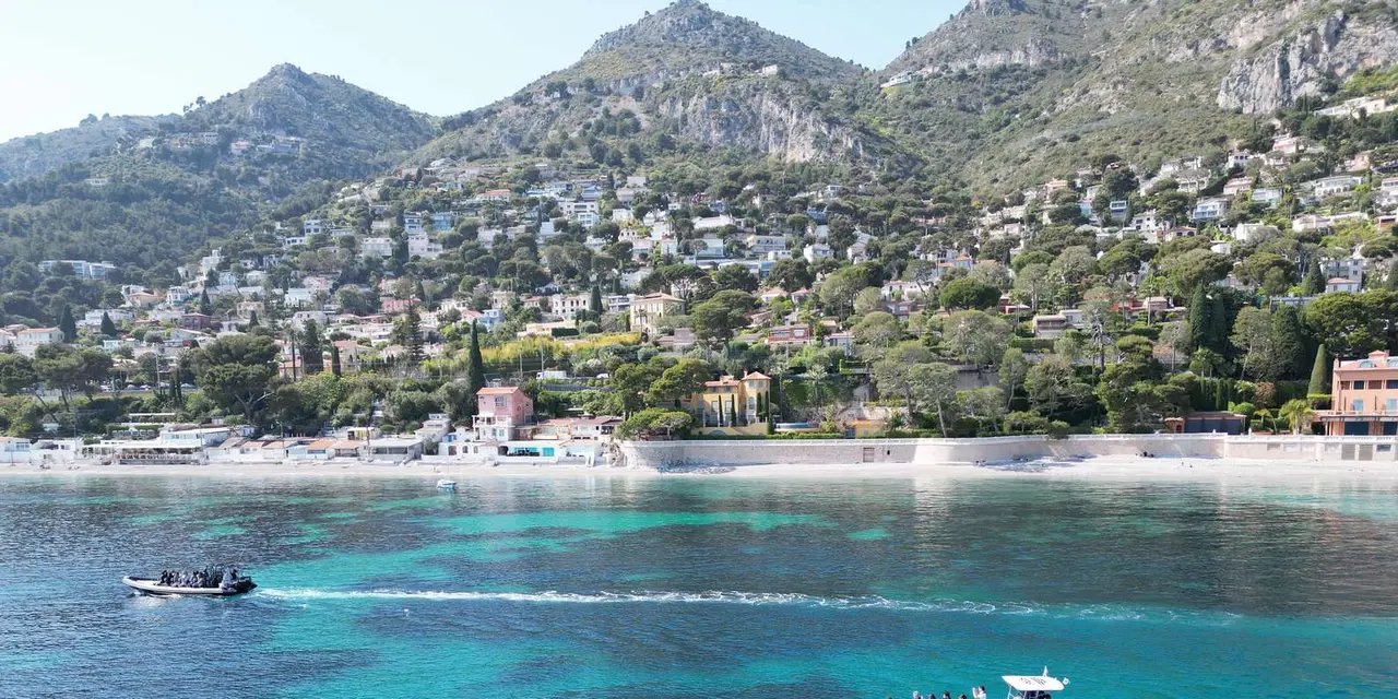 Two speedboats crossing bright turquoise water below a hillside town on the Riviera
