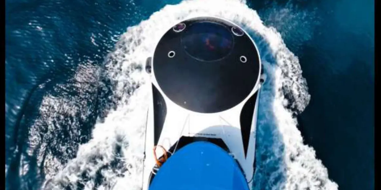 Overhead view of a white boat with a clear viewing dome cutting through dark-blue water