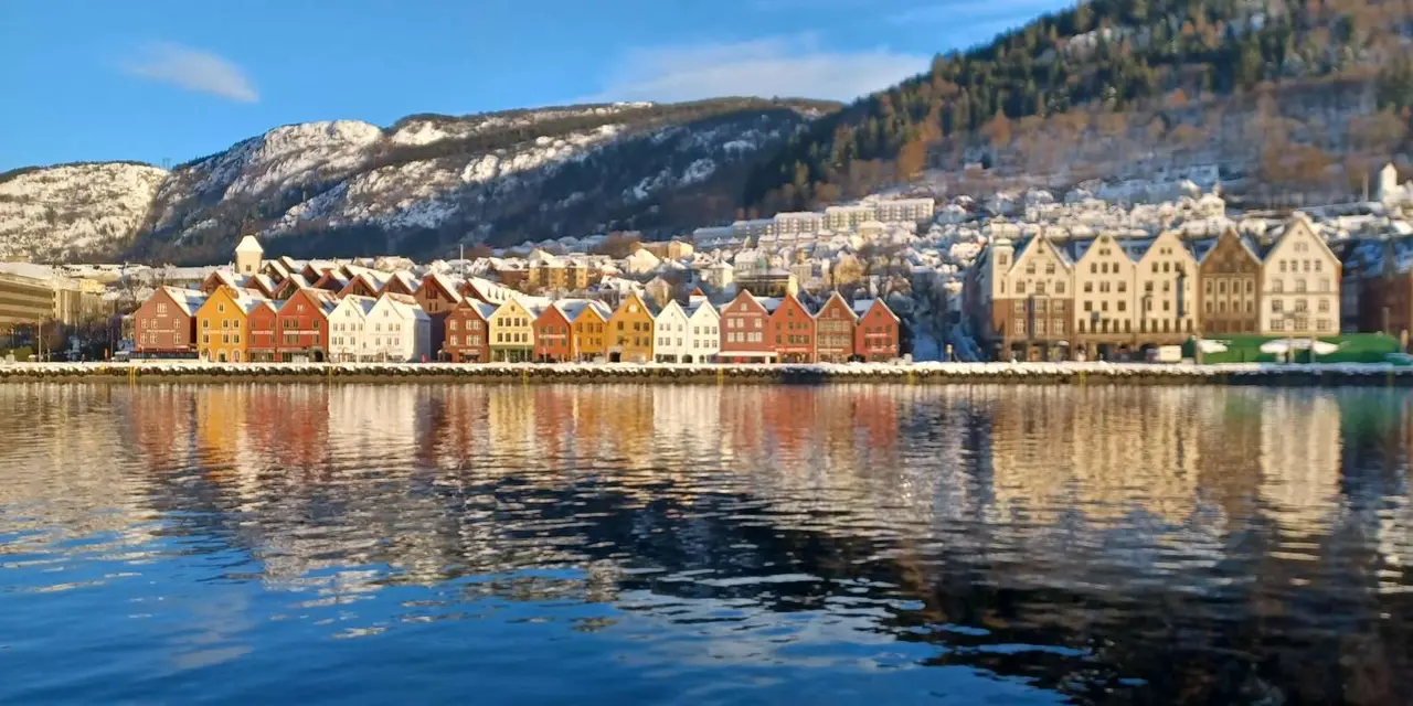 Bryggen's row of coloured wooden wharf houses reflected in the still harbour below wooded hills