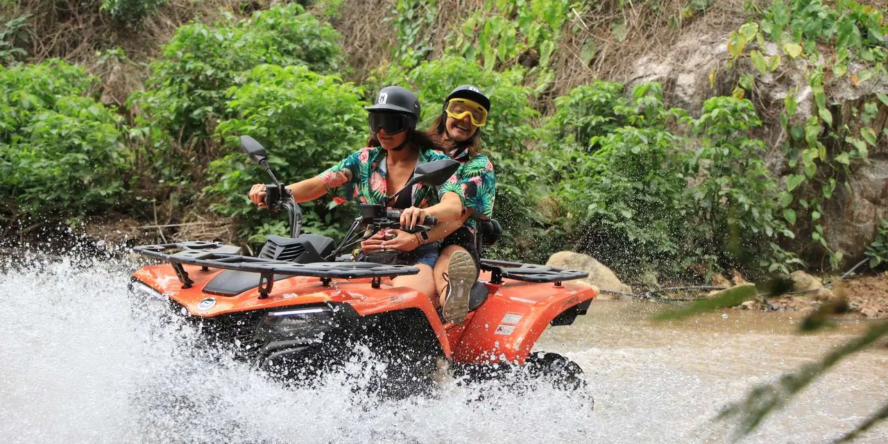 Two riders in helmets and goggles on an orange ATV splashing through a shallow river
