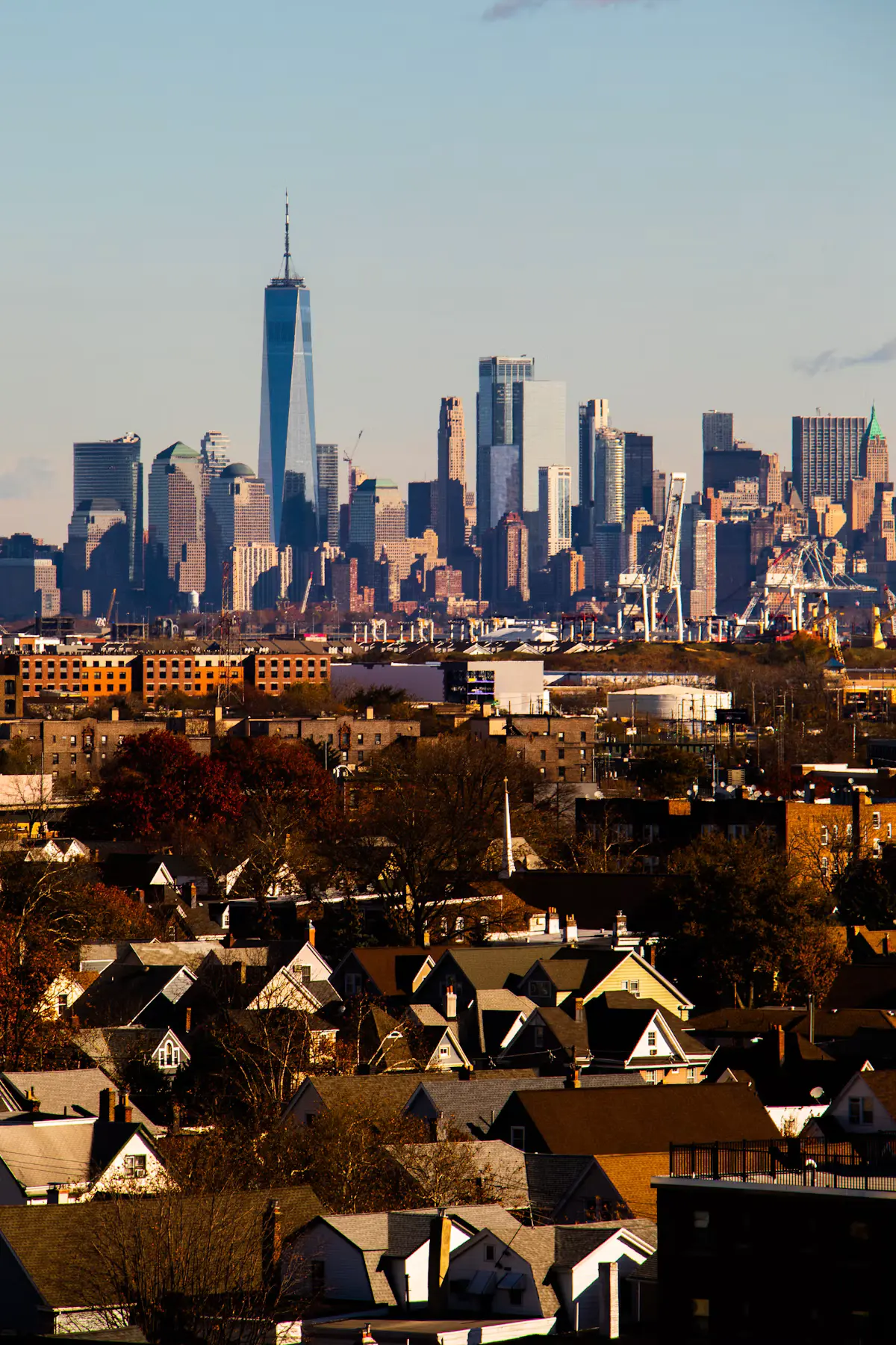 The lower Manhattan skyline with One World Trade Center, seen over the rooftops and port cranes of Bayonne on a clear blue day