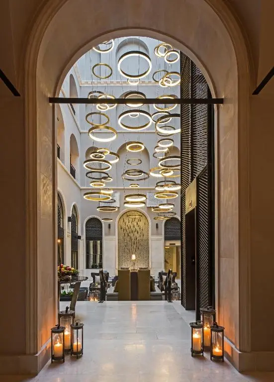 Arched entrance to 10 Karaköy's lobby, lit by lanterns, with a cascade of golden ring chandeliers hanging in the hall beyond