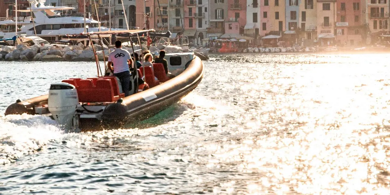 A speedboat with passengers crossing the water in front of Portovenere's colourful harbour houses