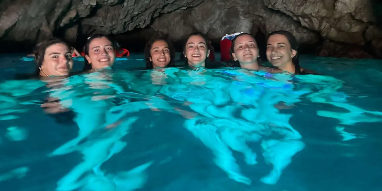 A group of smiling swimmers in turquoise water inside a dark sea cave
