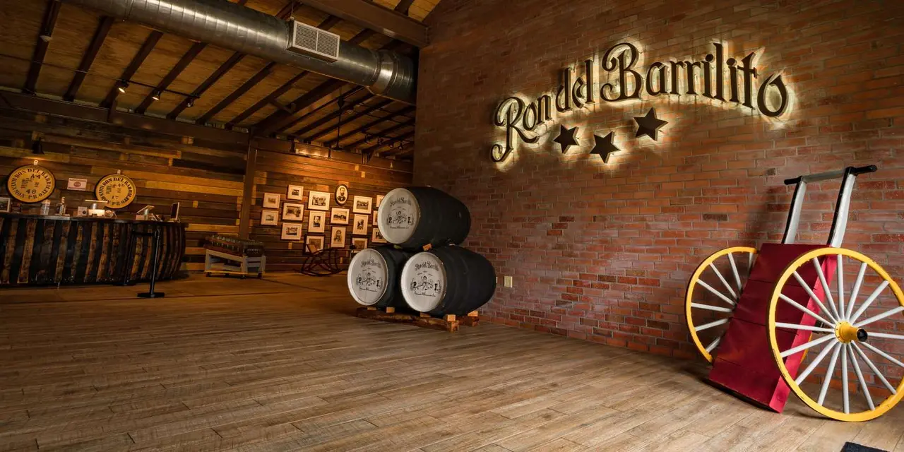 A wall sign reading Ron del Barrilito above oak rum barrels and a wooden cart wheel