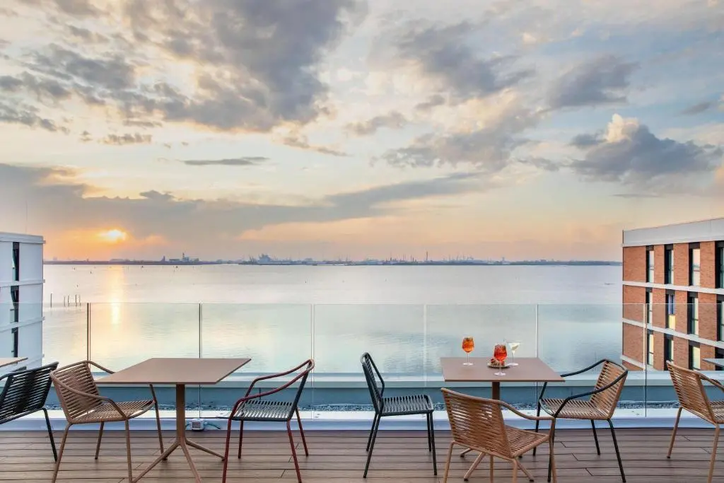 Rooftop terrace of B&B HOTEL Venezia Laguna with tables and chairs and spritz drinks looking out over the lagoon at sunset