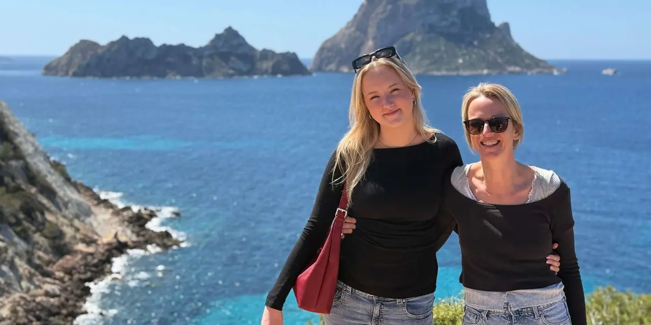 Two women posing on a clifftop with the rock of Es Vedrà and a smaller island behind them over deep blue water
