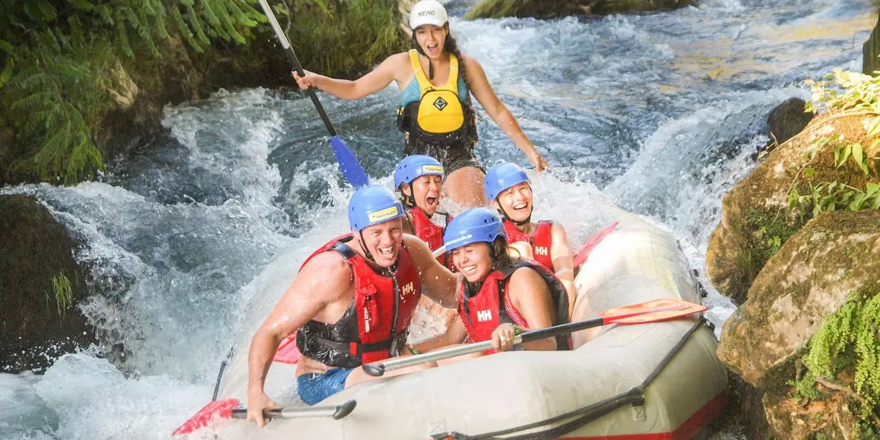 Rafters in helmets and life vests paddling through white water in a green canyon